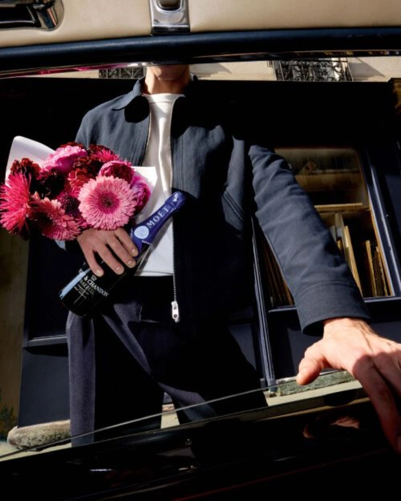 Persoon stapt uit auto met roze boeket en fles Moët & Chandon champagne Midnight Blue in de hand